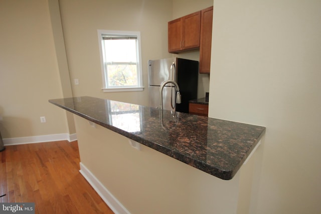 kitchen featuring light wood-type flooring, stainless steel fridge, a breakfast bar, and kitchen peninsula