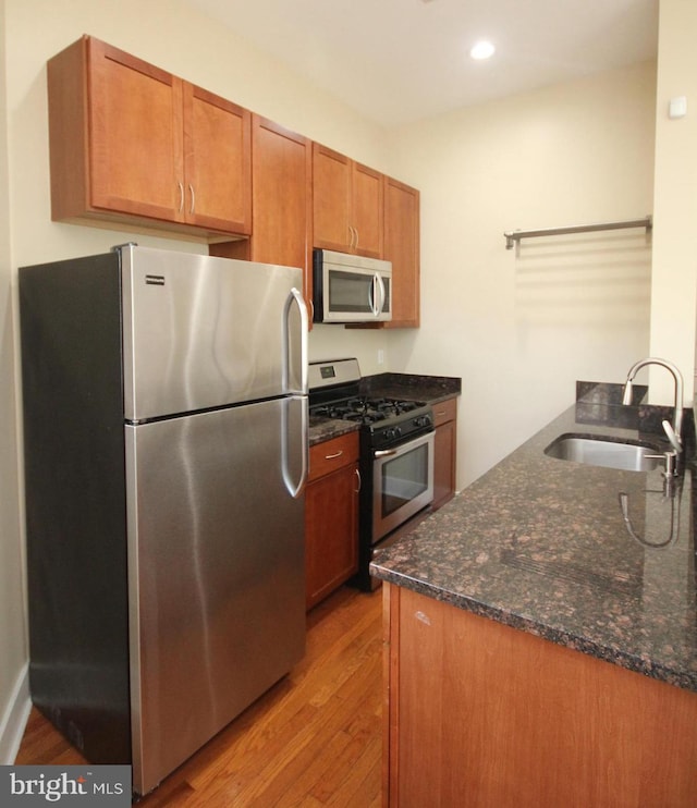 kitchen featuring light wood-type flooring, appliances with stainless steel finishes, sink, and dark stone countertops