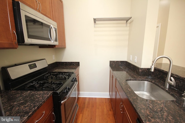 kitchen featuring light wood-type flooring, dark stone counters, sink, and black gas range