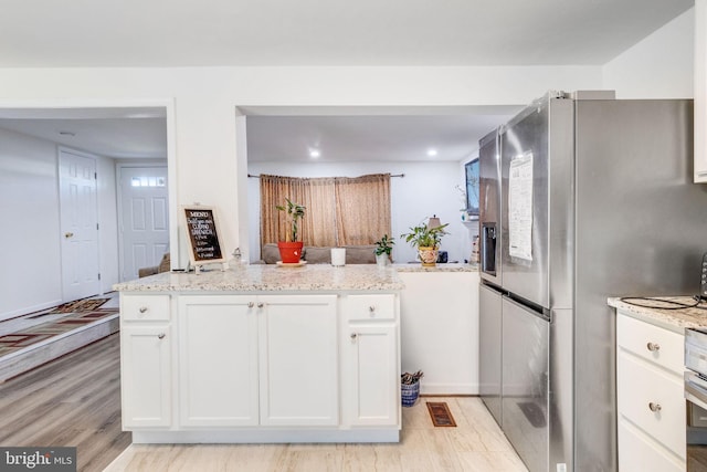 kitchen with white cabinets, light wood-type flooring, light stone counters, and stainless steel fridge