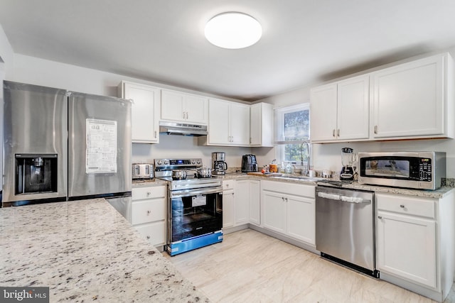 kitchen with white cabinets, appliances with stainless steel finishes, sink, and light stone countertops