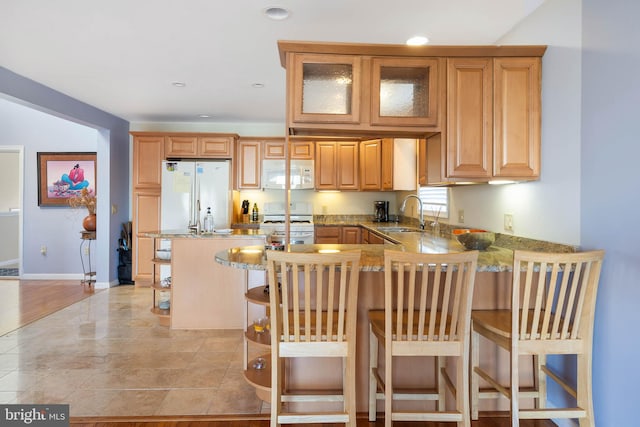 kitchen featuring a kitchen bar, kitchen peninsula, sink, and white appliances