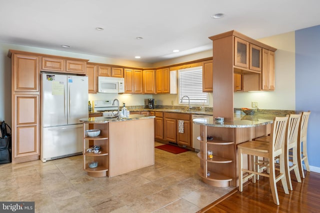 kitchen featuring light stone counters, kitchen peninsula, sink, a breakfast bar, and white appliances