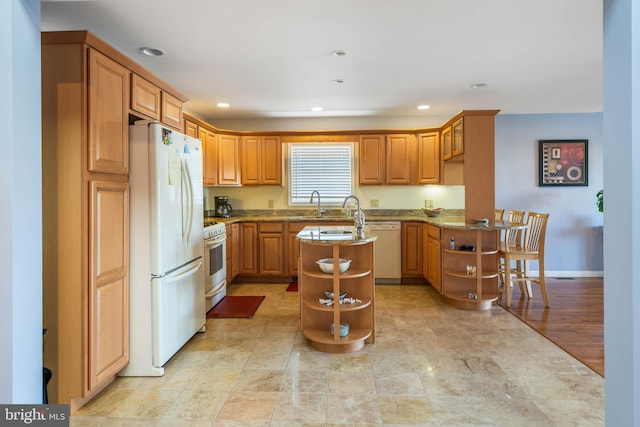 kitchen with light stone counters, a breakfast bar area, white appliances, light hardwood / wood-style flooring, and a center island