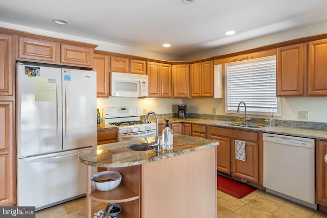 kitchen with white appliances, sink, light stone counters, and a center island with sink