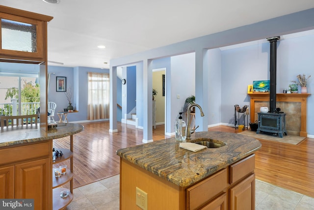 kitchen with light hardwood / wood-style floors, dark stone counters, a wood stove, sink, and a kitchen island with sink