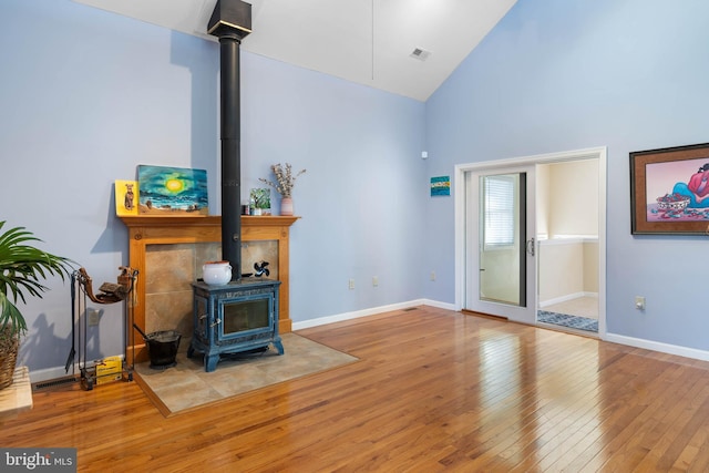 living room with light wood-type flooring, a wood stove, and high vaulted ceiling