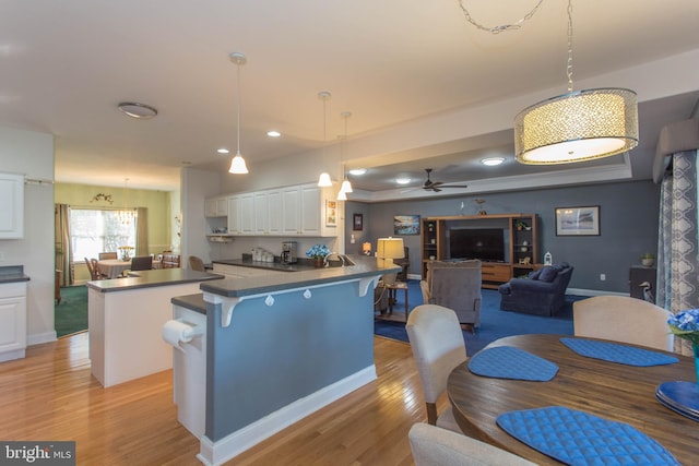 kitchen featuring white cabinets, kitchen peninsula, ceiling fan, light hardwood / wood-style flooring, and decorative light fixtures