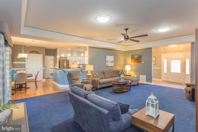 living room with hardwood / wood-style flooring, ceiling fan, crown molding, and a tray ceiling