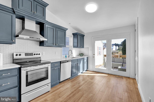 kitchen with tasteful backsplash, stainless steel appliances, wall chimney range hood, light hardwood / wood-style floors, and lofted ceiling