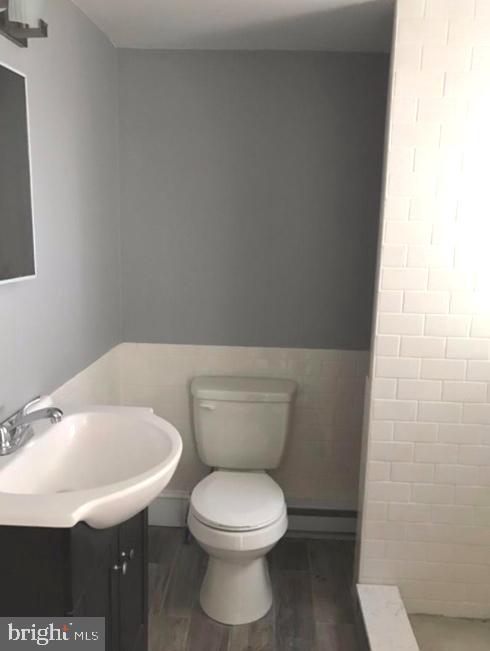 bathroom with wood-type flooring, vanity, toilet, and tile walls