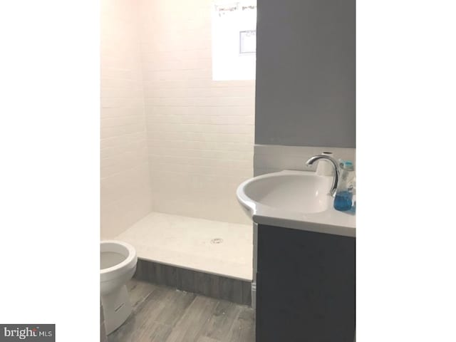 bathroom featuring toilet, tiled shower, vanity, tile walls, and hardwood / wood-style flooring