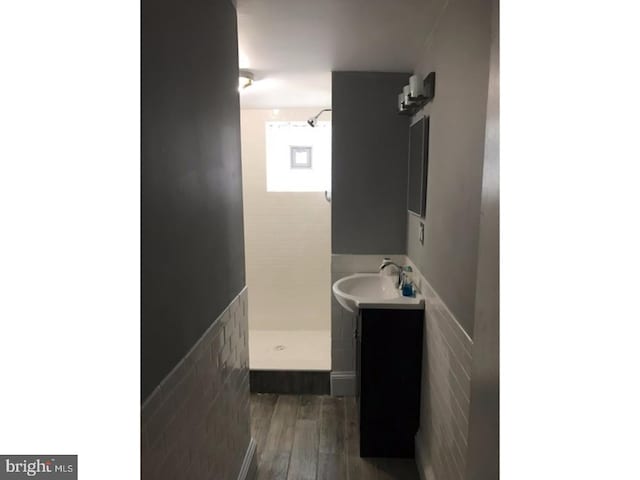 bathroom featuring a shower, hardwood / wood-style floors, vanity, and tile walls