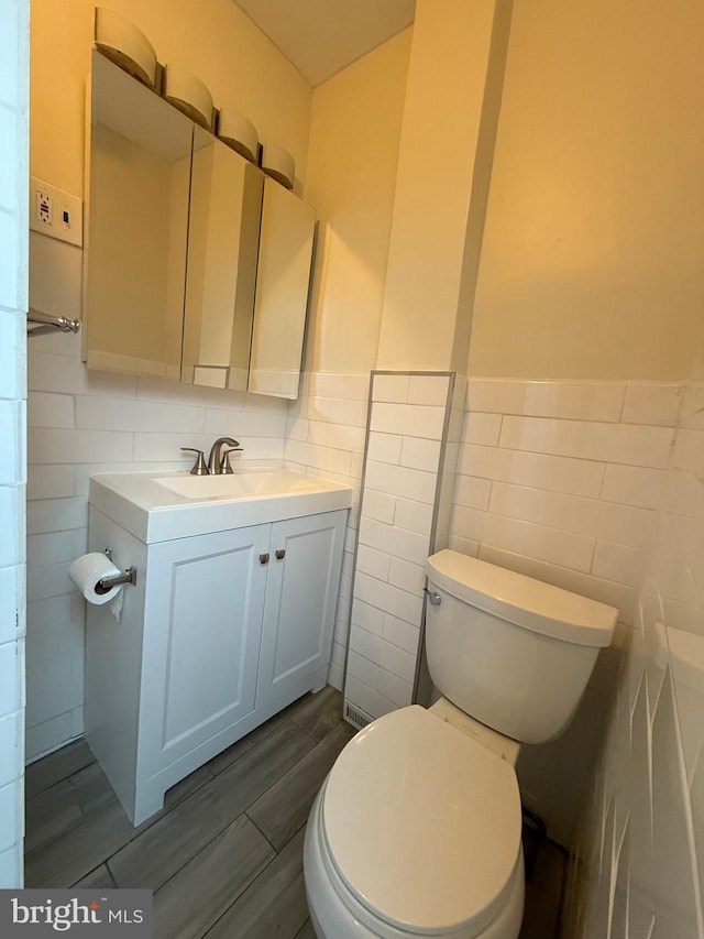 bathroom featuring wood-type flooring, vanity, toilet, and tile walls