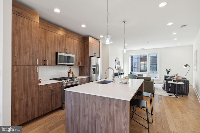 kitchen featuring sink, hanging light fixtures, stainless steel appliances, light hardwood / wood-style floors, and a kitchen island with sink