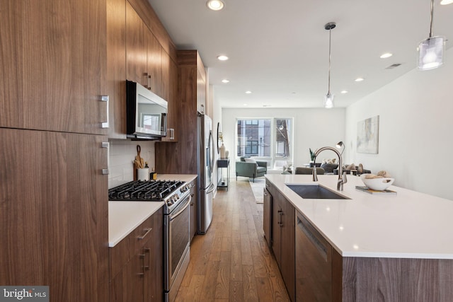 kitchen with hanging light fixtures, sink, stainless steel appliances, and wood-type flooring