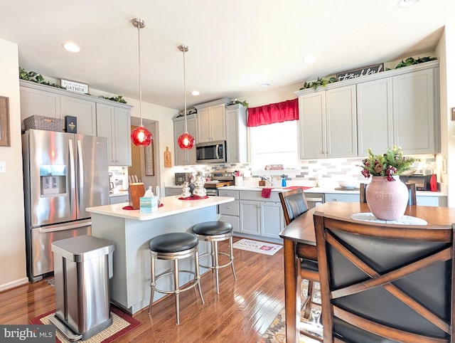 kitchen with gray cabinets, appliances with stainless steel finishes, decorative light fixtures, a breakfast bar area, and a center island