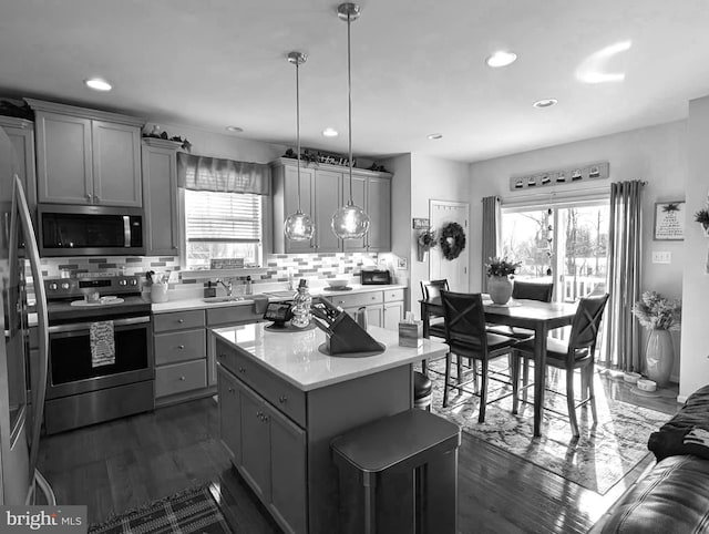 kitchen featuring gray cabinets, appliances with stainless steel finishes, hanging light fixtures, a kitchen island, and decorative backsplash