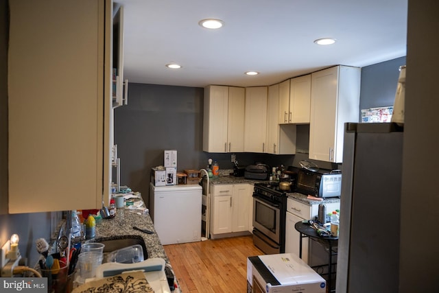 kitchen featuring light wood-style floors, stainless steel gas range oven, dark stone countertops, recessed lighting, and white cabinets