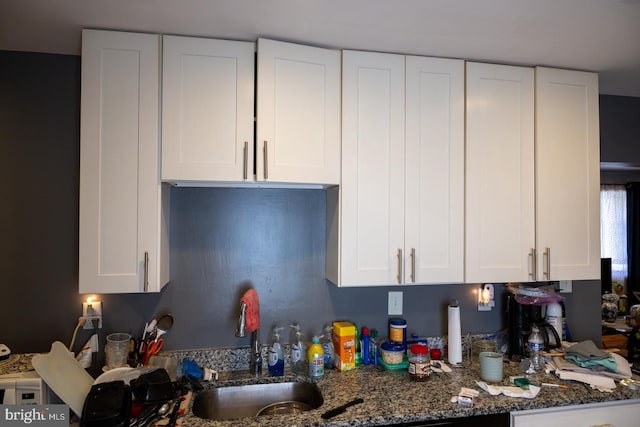 kitchen with white cabinets, a sink, and dark stone countertops
