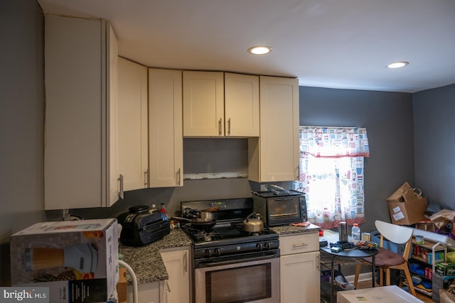 kitchen with stainless steel gas range, white cabinetry, stone counters, and recessed lighting