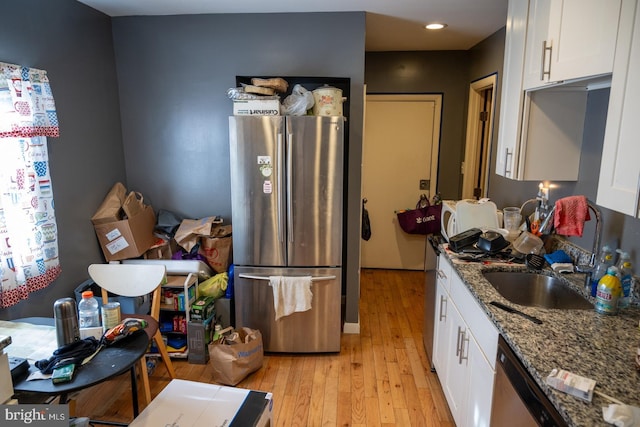 kitchen featuring appliances with stainless steel finishes, light wood-style floors, white cabinetry, stone countertops, and a sink