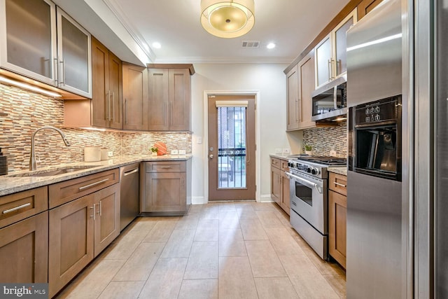 kitchen with light stone counters, sink, crown molding, backsplash, and appliances with stainless steel finishes