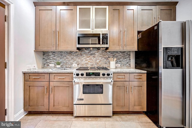 kitchen with appliances with stainless steel finishes, light tile patterned flooring, backsplash, and light stone countertops