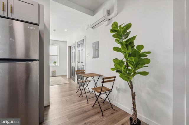 corridor with light wood finished floors, a wall mounted air conditioner, electric panel, baseboards, and recessed lighting