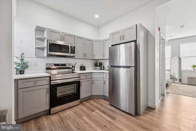 kitchen with appliances with stainless steel finishes, gray cabinets, backsplash, light wood-type flooring, and recessed lighting