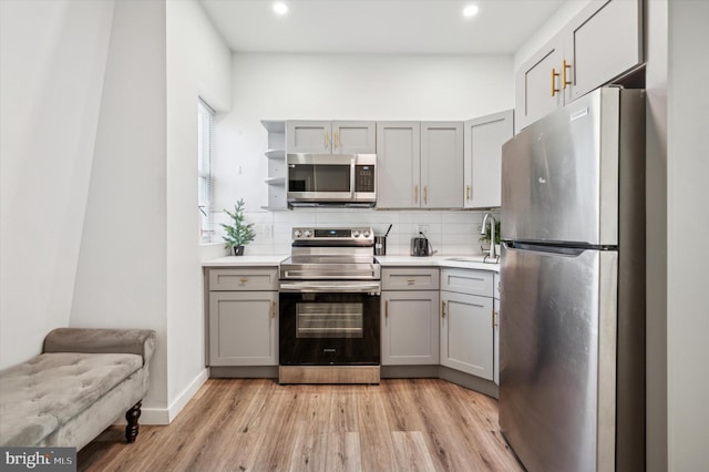 kitchen featuring stainless steel appliances, gray cabinets, a sink, light wood-type flooring, and decorative backsplash
