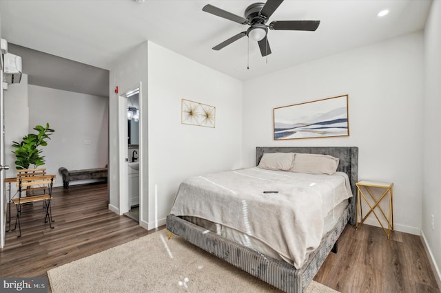 bedroom featuring a wall mounted air conditioner, wood-type flooring, connected bathroom, and ceiling fan