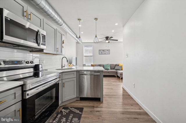 kitchen with appliances with stainless steel finishes, a sink, gray cabinets, ceiling fan, and a peninsula
