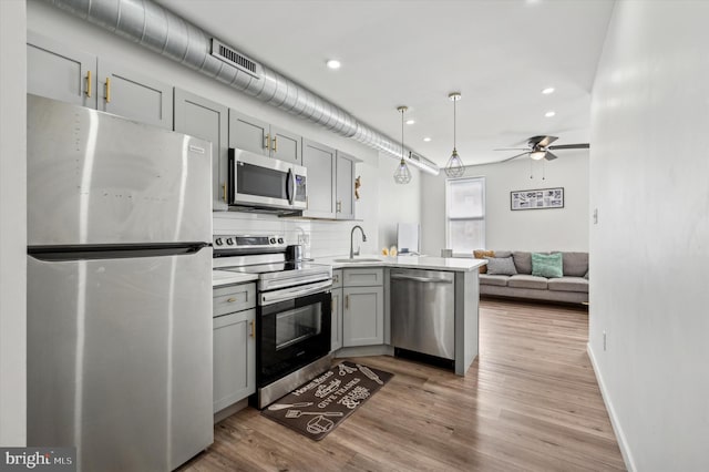 kitchen with stainless steel appliances, gray cabinets, a sink, a peninsula, and light wood-style flooring