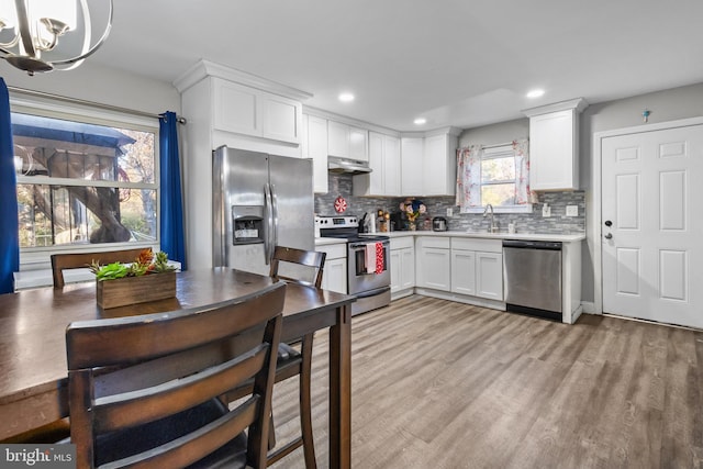 kitchen with light hardwood / wood-style flooring, hanging light fixtures, white cabinetry, appliances with stainless steel finishes, and range hood