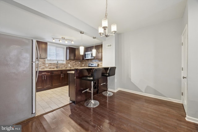 kitchen with hanging light fixtures, tasteful backsplash, light hardwood / wood-style floors, a breakfast bar, and dark brown cabinets