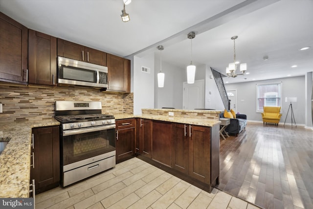 kitchen with kitchen peninsula, appliances with stainless steel finishes, light stone countertops, light hardwood / wood-style flooring, and hanging light fixtures