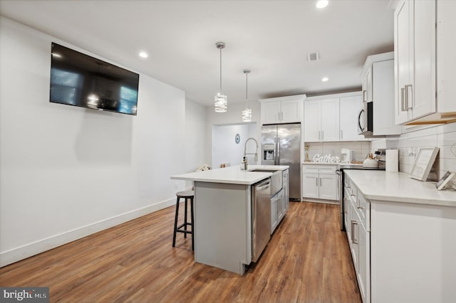 kitchen with white cabinets, stainless steel appliances, a kitchen island with sink, and hardwood / wood-style floors