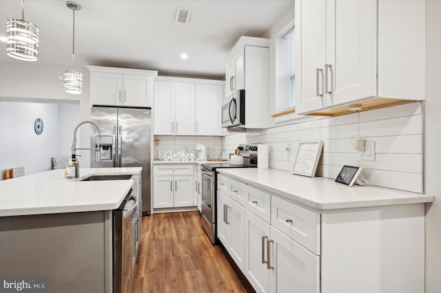 kitchen with white cabinetry, sink, hardwood / wood-style floors, pendant lighting, and appliances with stainless steel finishes