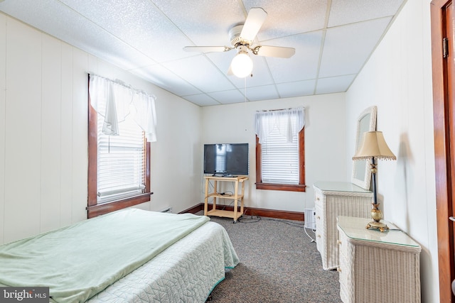 bedroom featuring a drop ceiling, dark colored carpet, and ceiling fan