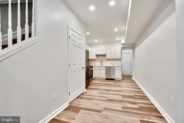 kitchen with light hardwood / wood-style floors, white cabinetry, sink, appliances with stainless steel finishes, and decorative backsplash