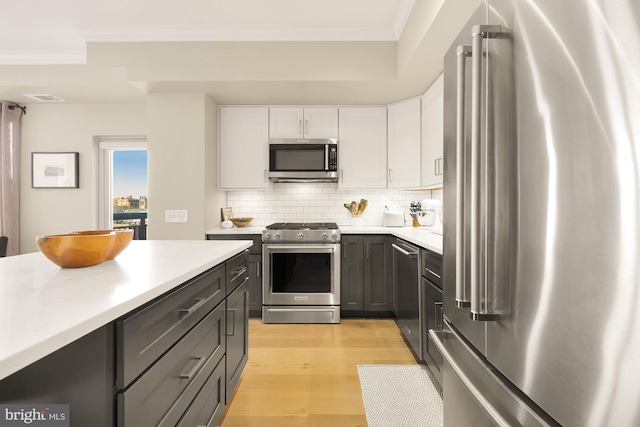 kitchen featuring white cabinetry, stainless steel appliances, light hardwood / wood-style flooring, crown molding, and decorative backsplash