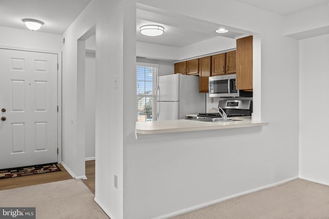 kitchen with kitchen peninsula, appliances with stainless steel finishes, sink, and light colored carpet