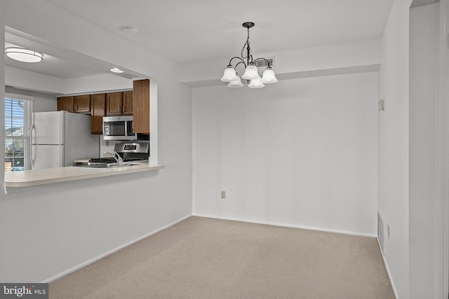 kitchen featuring stainless steel appliances, hanging light fixtures, light carpet, and a notable chandelier