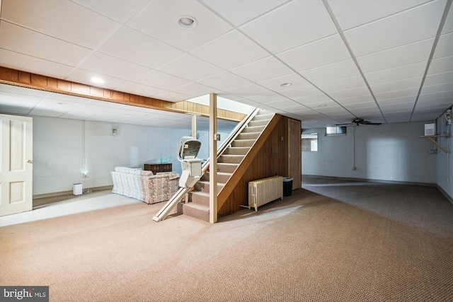 basement featuring a paneled ceiling, radiator heating unit, and carpet floors