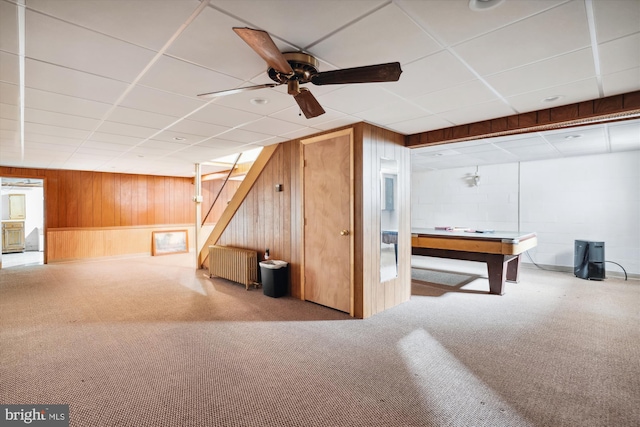 basement with radiator heating unit, wooden walls, ceiling fan, and carpet floors