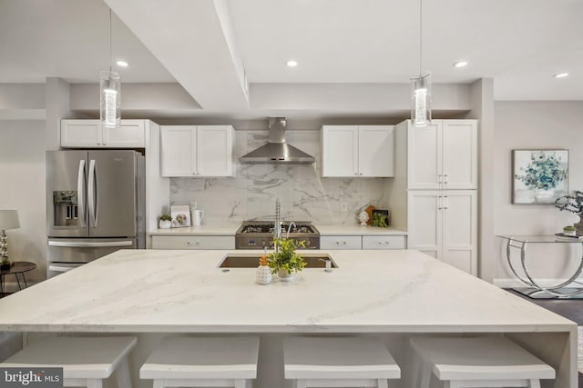 kitchen featuring white cabinets, stainless steel refrigerator with ice dispenser, wall chimney range hood, and decorative light fixtures