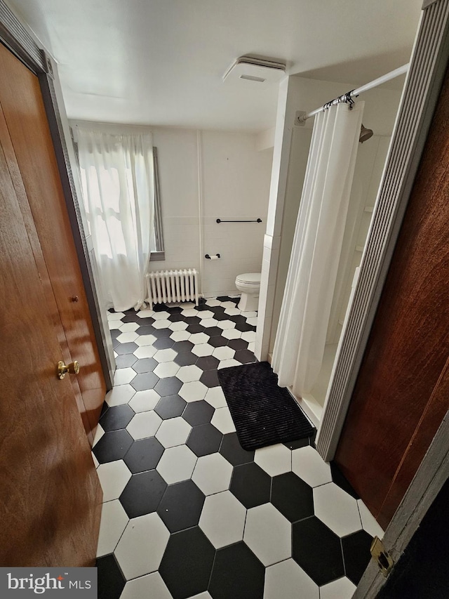 bathroom with a shower with curtain, radiator heating unit, and toilet