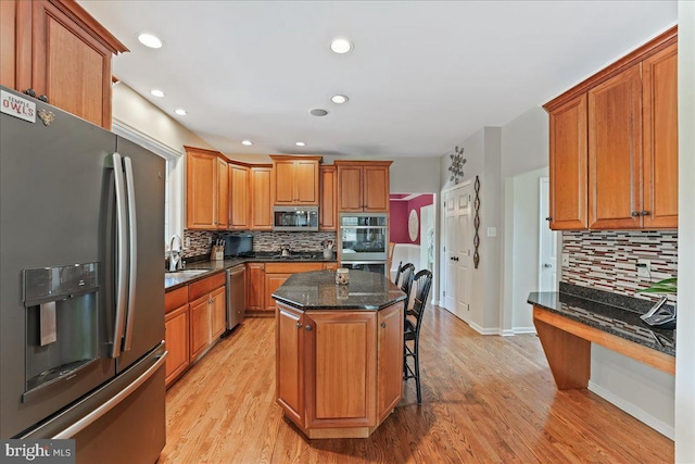 kitchen featuring stainless steel appliances, dark stone countertops, light wood-type flooring, and a kitchen island