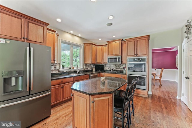 kitchen with light hardwood / wood-style floors, dark stone countertops, a kitchen island, and appliances with stainless steel finishes